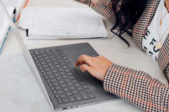 Frau sitzt am Tisch und arbeitet am Laptop.