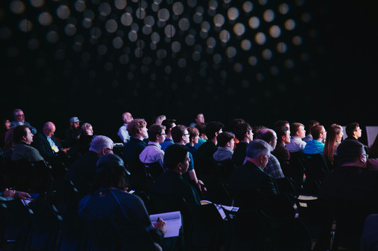 Menschen sitzen in Reihen und schauen auf die Bühne.