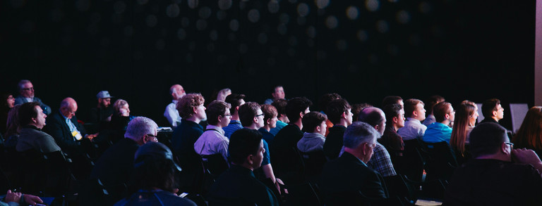 Menschen sitzen in Reihen und schauen auf die Bühne.
